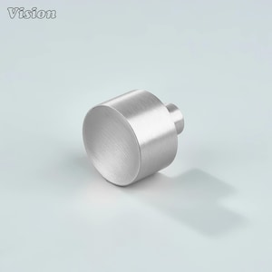 May include: A silver cabinet knob with a cylindrical body and a small, round stem. The knob has a brushed metal finish. The word "Vision" is in the top left corner.