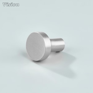 Puede incluir: Un pomo de armario de metal plateado cepillado con un vástago cilíndrico y una cabeza circular. La palabra "Vision" está en la esquina superior izquierda. El pomo está diseñado para muebles y decoración del hogar.