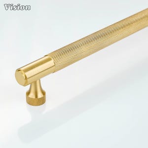Könnte beinhalten: Ein goldfarbener Schrankgriff mit rautenförmigem Griff. Der Griff hat eine zylindrische Form mit einem flachen Ende und einem dekorativen Sockel. Das Wort "Vision" befindet sich in der oberen linken Ecke.