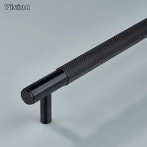 May include: A black cabinet pull with a cylindrical handle and a ribbed texture. The pull has a T-shaped design and is made of metal. The word "Vision" is in the upper left corner.