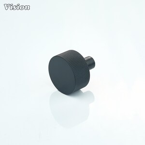 May include: A black cabinet knob with a textured, knurled grip and a smooth, circular face. The knob has a cylindrical post for mounting. The word "Vision" is in the upper left corner.