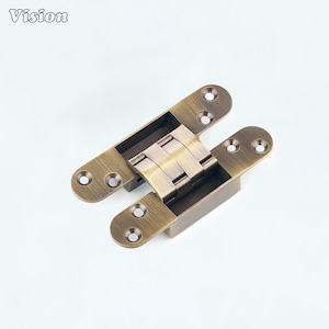 Pode incluir: Uma dobradiça oculta de metal na cor latão com acabamento escovado. A dobradiça apresenta duas placas de montagem alongadas, cada uma com dois orifícios circulares para parafusos, conectadas por um mecanismo de pivô central com três segmentos.