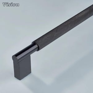 Peut inclure: Une poignée de meuble noire avec une poignée texturée à motif de losanges et une base rectangulaire. Le mot "Vision" est dans le coin supérieur gauche. La quincaillerie est conçue pour les meubles et la décoration intérieure.