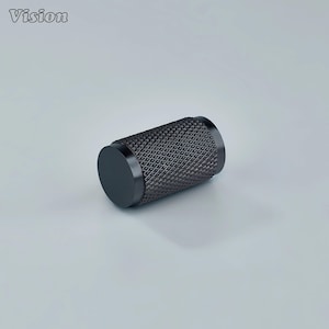 May include: A cylindrical, black metal object with a diamond pattern texture. The object has a flat, circular end cap on each side. The word "Vision" is printed in white in the upper left corner.