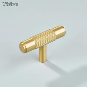 May include: A gold-colored T-bar cabinet pull with a cylindrical, ridged center section and a smooth, rounded end. The pull has a vertical post for mounting. The word "Vision" is in the upper left corner.