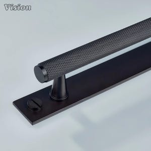 Peut inclure: Une poignée de porte noire avec une poignée à motif de losanges et une base rectangulaire. La poignée est cylindrique et montée sur une plaque noire avec une seule vis. Le mot "Vision" est dans le coin supérieur gauche.