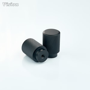 May include: Two black cylindrical knobs with a textured diamond pattern. One knob is lying on its side, while the other stands upright. The word "Vision" is in the upper left corner.