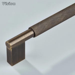 May include: Bronze-toned cabinet pull with a diamond-patterned handle. The pull features a rectangular base and a cylindrical handle with a textured surface. The word "Vision" is in the upper left corner.
