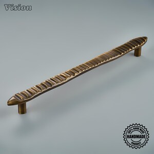 May include: A long, horizontal cabinet pull handle with a dark antique brass finish. The handle features a textured, repeating scalloped or ribbed pattern along its entire length and is supported by two cylindrical mounting posts at each end.