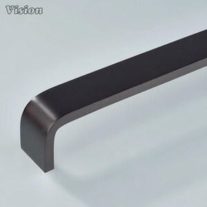 Pode incluir: Um puxador de móvel preto fosco com um design curvo em forma de U suave. A ferragem apresenta um perfil retangular sólido com bordas arredondadas e um acabamento limpo e uniforme. A palavra Vision está impressa no canto superior esquerdo.