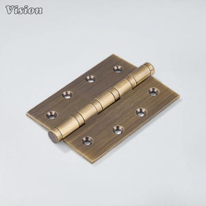 May include: A bronze-colored door hinge with a rectangular shape and rounded edges. The hinge has multiple screw holes and a cylindrical barrel in the center. The word "Vision" is in the top left corner.