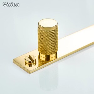 May include: A gold-colored cabinet pull with a textured cylindrical handle and a flat rectangular base. A small screw is visible on the base. The word "Vision" is in the upper left corner.