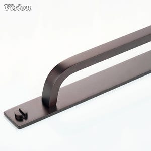 May include: A dark bronze-colored door pull with a curved handle and a rectangular base. The word "Vision" is printed in the upper left corner. The base has a screw head on the end.