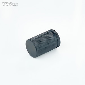 May include: A black cylindrical object with a textured surface and a flat, circular end. The object has a smaller, raised section at one end. The word "Vision" is in the upper left corner.