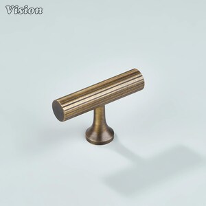 May include: A bronze-colored cabinet pull with a cylindrical handle featuring horizontal grooves. The pull has a T-shaped design with a round base. The word "Vision" is in the upper left corner.