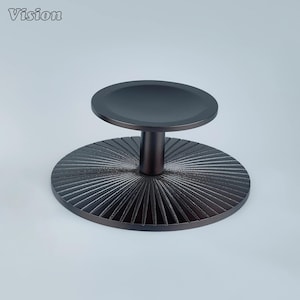 May include: A dark bronze-colored decorative stand with a circular top and a base with a radial design. The stand has a short, cylindrical stem connecting the top and base. The word "Vision" is in the top left corner.