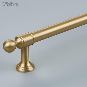 May include: A brushed brass cabinet handle featuring a cylindrical bar, a spherical finial at the end, and a sturdy mounting post with a flared base. The metal surface has a matte, textured finish that reflects light evenly across the hardware.