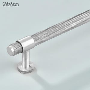以下が含まれることがあります： ダイヤモンド模様のグリップが付いたシルバーのキャビネットプル。 プルは円筒形のハンドルと円形のベースを備えています。 「Vision」という言葉が左上にあります。 このハードウェアは、キッチンまたはバスルームのキャビネットに適しています。