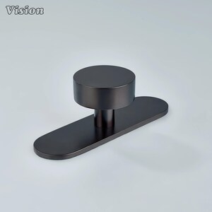 May include: A dark gray cabinet knob with a cylindrical top and a rectangular base. The knob has a modern design and is made of metal. The word "Vision" is in the top left corner.