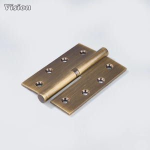 May include: A bronze-colored door hinge with a cylindrical barrel and rectangular leaves. Each leaf has multiple circular holes for screws. The word "Vision" is printed in the upper left corner.