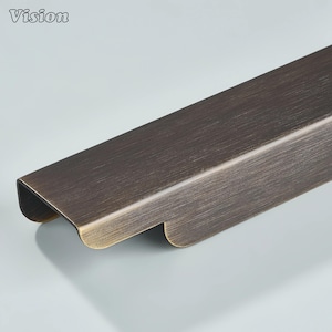 May include: A bronze-colored cabinet pull with a rectangular shape and rounded edges. The pull has a brushed metal finish and the word "Vision" is in the upper left corner.