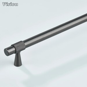 May include: A dark gray cabinet pull with a textured, diamond-patterned grip. The cylindrical handle extends into a smooth, straight bar. The Vision logo is in the upper left corner. This hardware is suitable for drawers and cabinets.