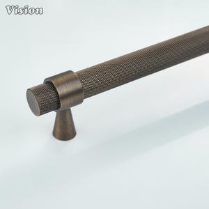 May include: A long, cylindrical cabinet handle with a dark bronze finish and a textured, cross-hatched knurled pattern. The handle features a smooth, circular mounting collar and a tapered, conical base that connects to the main bar.