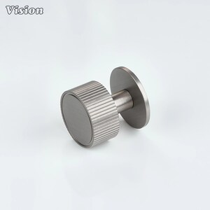 May include: A brushed metal cabinet knob with a circular base and a cylindrical handle with grooved detailing. The knob has a matte finish and is designed for furniture hardware.