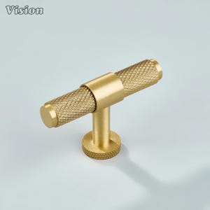 Op de afbeelding: Een goudkleurige kastgreep met een getextureerde, diamantpatroon handgreep. De greep heeft een cilindrische handgreep en een ronde basis. Het woord "Vision" staat in de linkerbovenhoek. Geschikt voor kasten en lades.