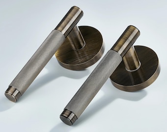 May include: Two antique bronze door handles with a textured grip and round backplates. The handles are cylindrical with a diamond pattern, and the backplates are circular. The Vision logo is in the top left corner.
