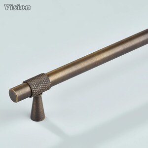 May include: A bronze cabinet pull with a diamond-patterned handle. The cylindrical bar and conical base are also bronze. The word "Vision" is visible in the top left corner.