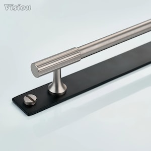 May include: A modern towel bar with a brushed nickel finish. The bar is mounted on a black rectangular base with a single screw. The word "Vision" is in the upper left corner.