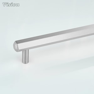 Könnte beinhalten: Ein gebürsteter silberner Schrankgriff mit einem geometrischen, sechseckigen Design. Der Griff hat einen zylindrischen Pfosten und einen langen, facettierten Griff. Das Wort "Vision" ist links oben aufgedruckt.