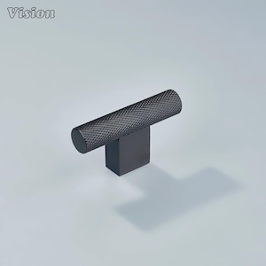 May include: A black cabinet knob with a textured, cylindrical handle and a square base. The word "Vision" is in the upper left corner. The knob is made of metal and casts a shadow on the light gray surface.