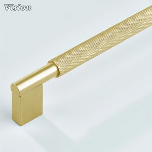 May include: A gold-coloured cabinet pull with a textured, diamond-patterned handle. The pull has a rectangular base and a cylindrical end. The word "Vision" is in the upper left corner.