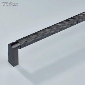 May include: A black cabinet pull with a textured, diamond-patterned grip. The handle has a rectangular end and a cylindrical body. The word "Vision" is in the upper left corner. This modern hardware is suitable for drawers and cabinets.