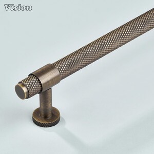 May include: Bronze-toned cabinet pull with a diamond-patterned grip. The pull features a cylindrical bar with a textured surface, a circular base, and a cylindrical post. The word "Vision" is in the upper left corner.