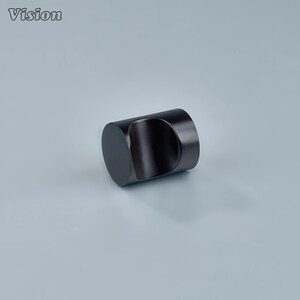 May include: A dark brown cylindrical cabinet knob with a curved, recessed grip. The knob has a smooth, matte finish and is set against a light blue-gray background. The word "Vision" is in the upper left corner.