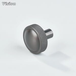 May include: A dark gray cabinet knob with a textured, diamond-patterned edge and a smooth, rounded center. The knob has a cylindrical stem for attachment. The word "Vision" is in the upper left corner.
