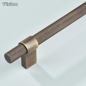 May include: Bronze cabinet pull with a diamond-patterned handle. The handle is cylindrical and attached to a square base. The word "Vision" is in the upper left corner. The hardware has an antique finish.