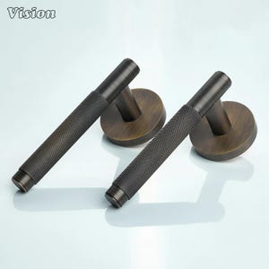 May include: Two bronze-toned door handles with a textured, diamond-patterned grip. Each handle has a circular base and a cylindrical grip. The word "Vision" is in the top left corner.
