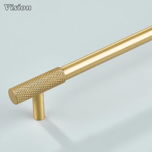 Può includere: Una maniglia per armadio color oro con un'impugnatura strutturata a forma di diamante. La maniglia ha un design cilindrico con una barra dritta e un montante verticale. La parola "Vision" è nell'angolo in alto a sinistra.