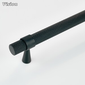 May include: Black cabinet pull with a textured, diamond-patterned grip. The pull has a cylindrical handle and a conical base. The word "Vision" is in the upper left corner. This hardware is suitable for drawers and cabinets.