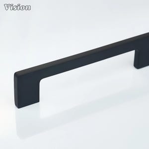 May include: A black cabinet pull handle with a rectangular bar and a squared-off handle. The word "Vision" is in the upper left corner. The handle is designed for easy gripping and is likely for a drawer or cabinet.