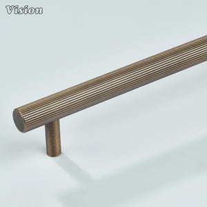 May include: Bronze-coloured cabinet pull with a ribbed design. The pull has a cylindrical handle and a short, cylindrical post. The word "Vision" is in the upper left corner. Suitable for drawers and cabinets.