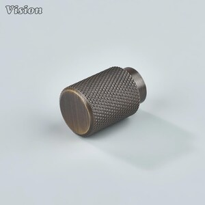 May include: A bronze-colored cabinet knob with a diamond-patterned texture. The cylindrical knob has a flat, circular end and a smaller, cylindrical base. The word "Vision" is in the upper left corner.
