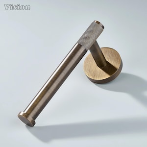 May include: A bronze-toned toilet paper holder with a textured handle and a circular wall mount. The holder has a cylindrical design and is made of metal. The word "Vision" is in the upper left corner.