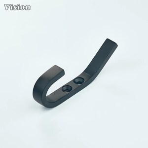 Könnte beinhalten: Ein mattschwarzer Wandhaken mit geschwungenem Design. Der Haken hat zwei vorgebohrte Löcher zur Montage. Das Wort "Vision" befindet sich in der oberen linken Ecke. Geeignet für Mäntel, Hüte oder andere Gegenstände.