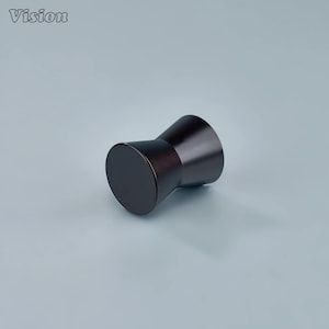 Op de afbeelding: Een donkerbruine kastknop in zandloper vorm met een matte afwerking. De knop heeft een cilindrische basis en bovenkant, verbonden door een taps toelopend middengedeelte. Het woord "Vision" staat in de linkerbovenhoek.