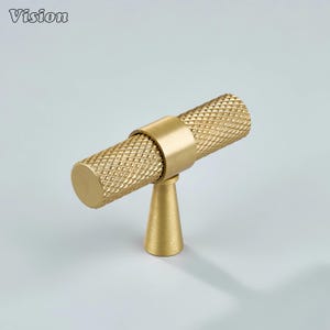 May include: A gold-colored cabinet knob with a textured, diamond-patterned cylindrical handle. The handle is connected to a round base by a ring and a conical stem. The word "Vision" is in the top left corner.